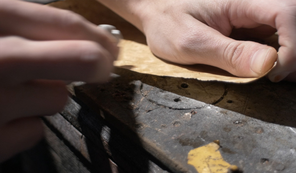 A pair of hands distressing the edges of the parchment paper. 