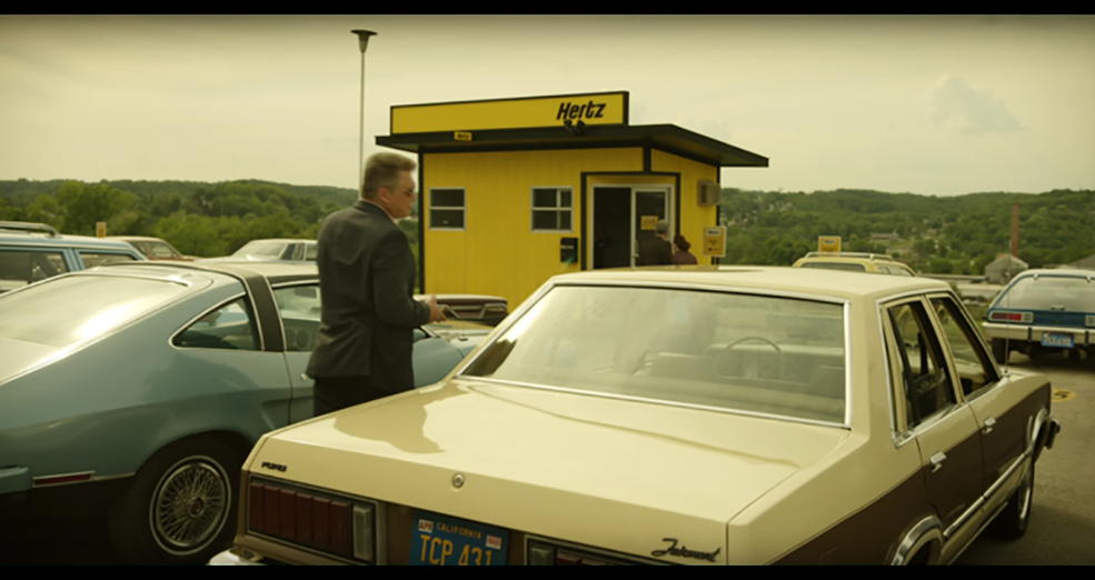 Still image from the film Mindhunter of a man walking between two parked cars. 