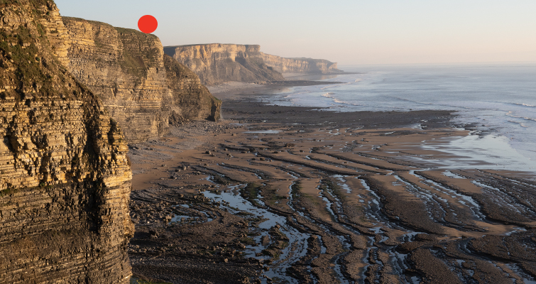 Landscape image of coastal cliffs with a red dot on top of the cliff edge indicating a specific location. 