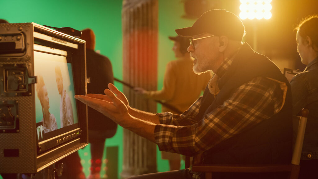 Male director in a film studio making a frustrated gesture towards a monitor screen displaying two actors