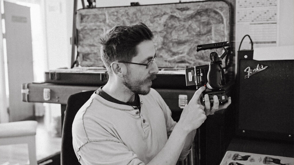 A bearded male holding the RED KOMODO and pointing to the record button.