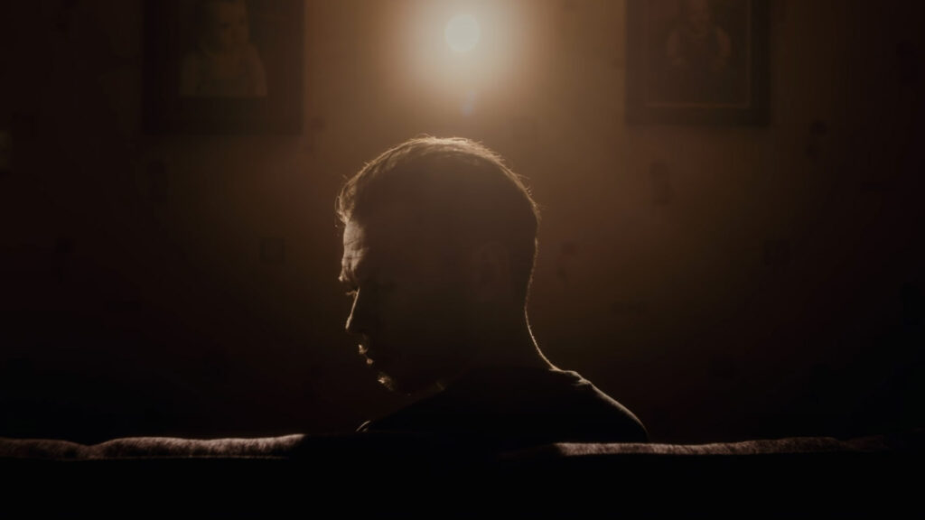 A man sitting in a dark room, illuminated by a rim light.