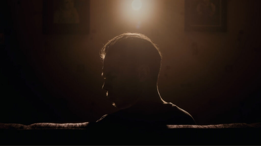 A man sitting in a dark room, illuminated by a rim light 